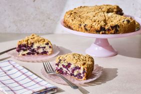 Blueberry buckle cake on a stand with two slices served on plates nearby