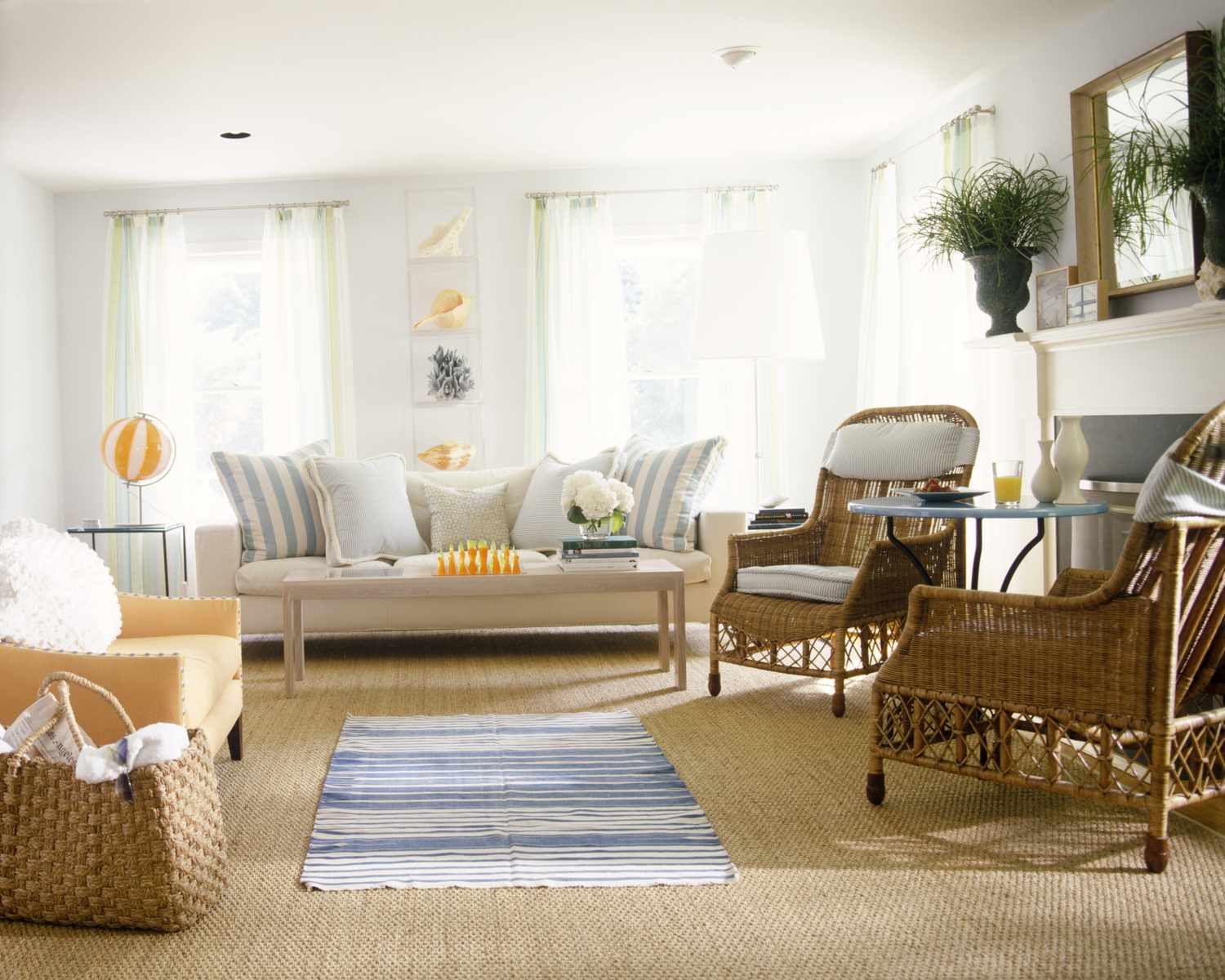 A cozy living room setup with wicker chairs a sofa and decor elements near windows and a fireplace