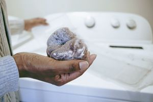 A hand holding clothes with detergent suds near a washing machine in the background