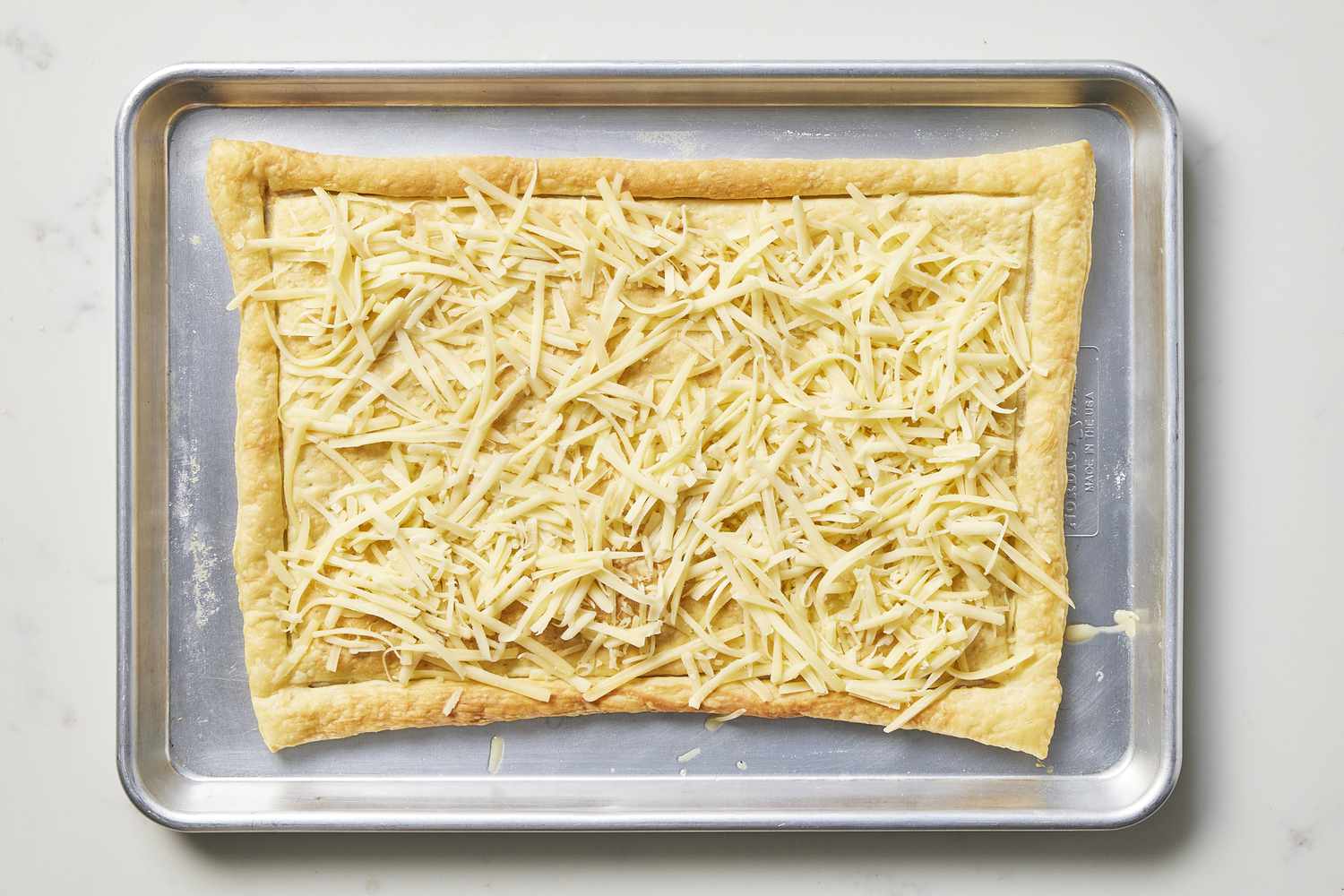 Baked pastry dough on a baking sheet topped with cheese
