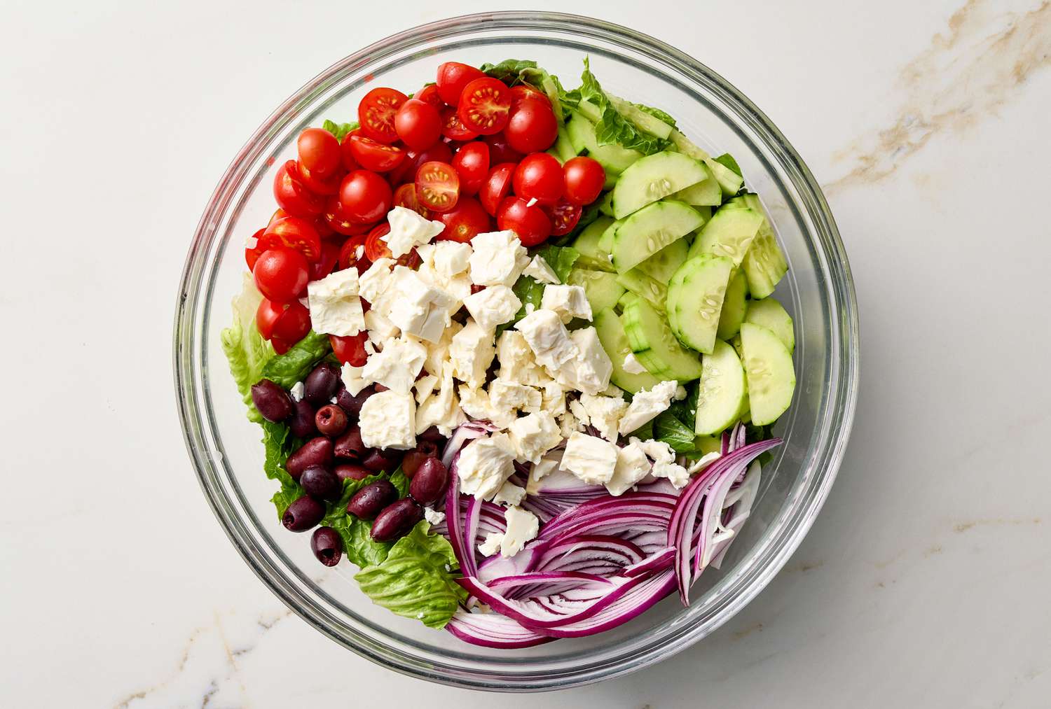 A Greek salad with ingredients including cherry tomatoes, cucumber slices, feta cheese, red onion, olives, and lettuce in a bowl