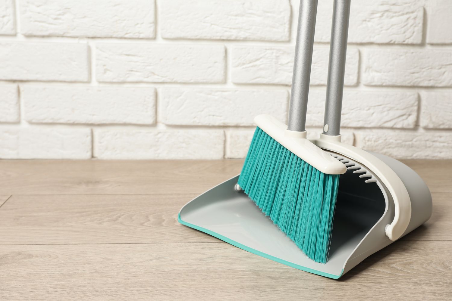 Plastic broom with dustpan near white brick wall indoors. Space for text