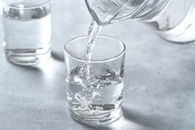 Water being poured from a pitcher into a glass with a second glass filled in the background