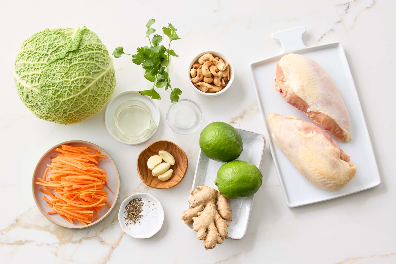 Ingredients including cabbage chicken breasts lime ginger cashews and more arranged on a countertop