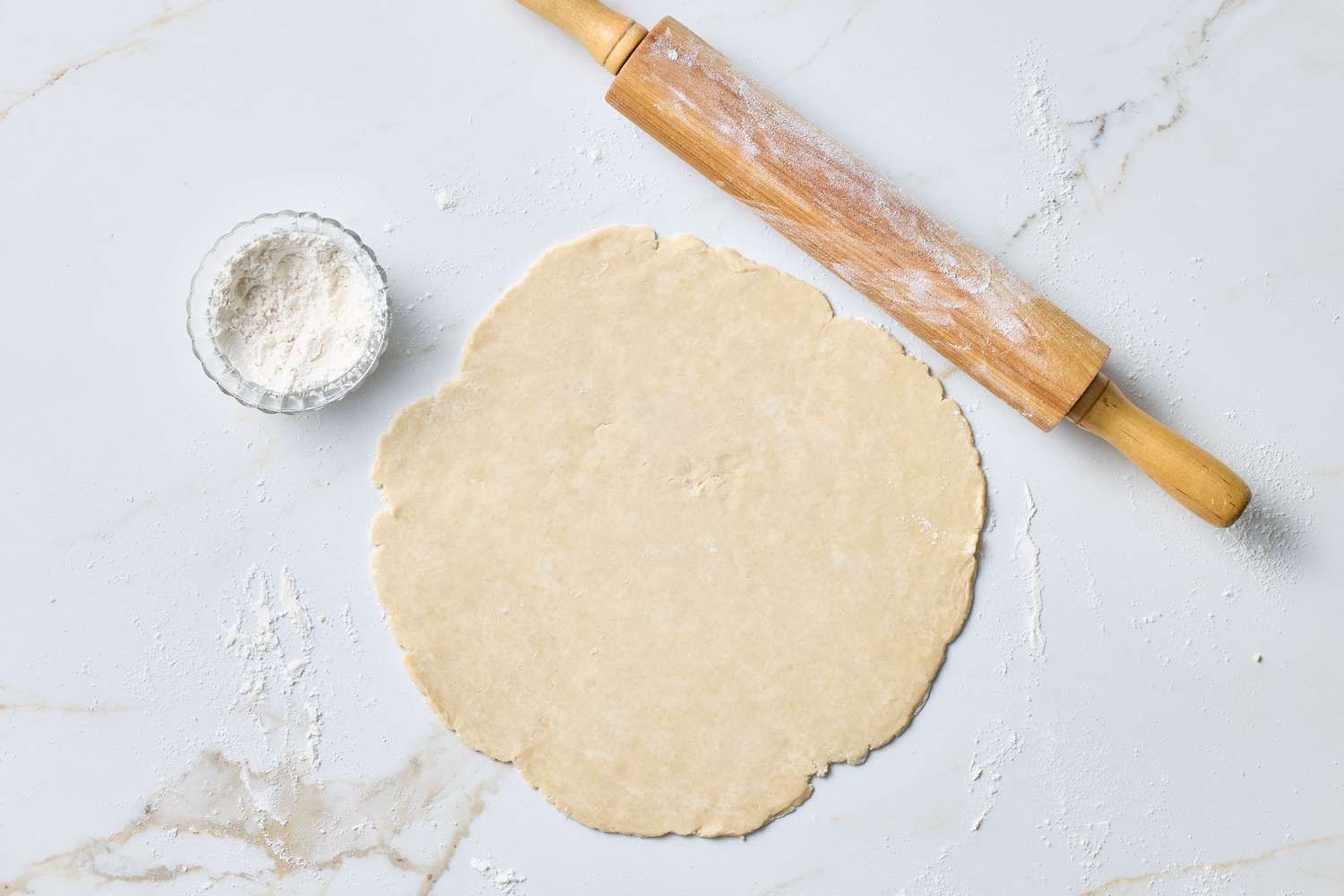 Rolled-out dough with flour and a rolling pin on a marble surface