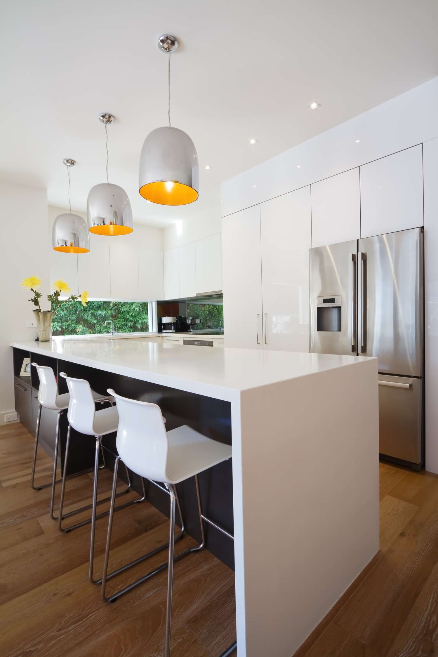 Modern kitchen interior with a white island four barstools pendant lighting and stainless steel appliances