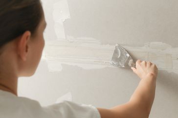 Person applying wallpaper or joint compound using a flat trowel