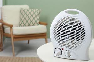 A portable space heater on a table with a chair and cushion in the background