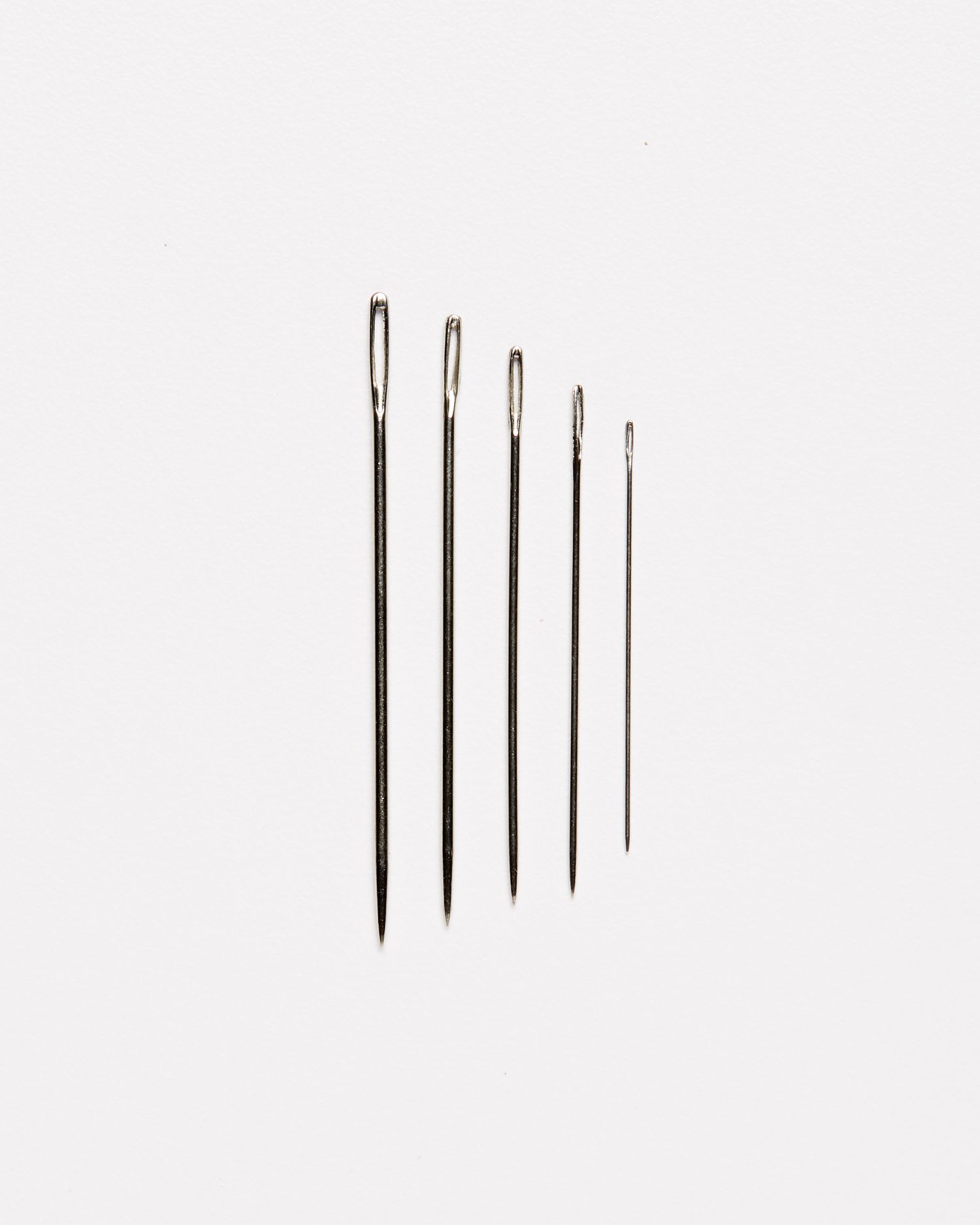 five various sizes of embroidery needles against a white background