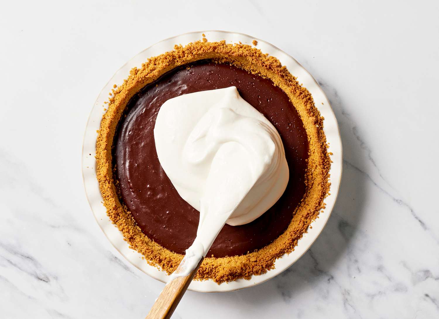 white meringue being spread on a chocolate pie