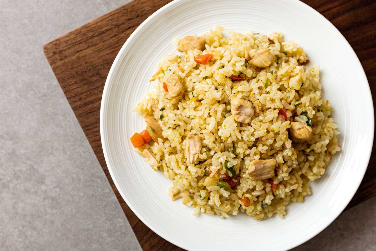 A plate of fried rice with chicken and vegetables on a table