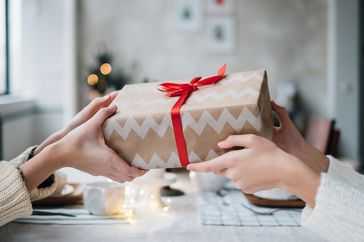 Two hands exchanging a wrapped gift across a table festive background