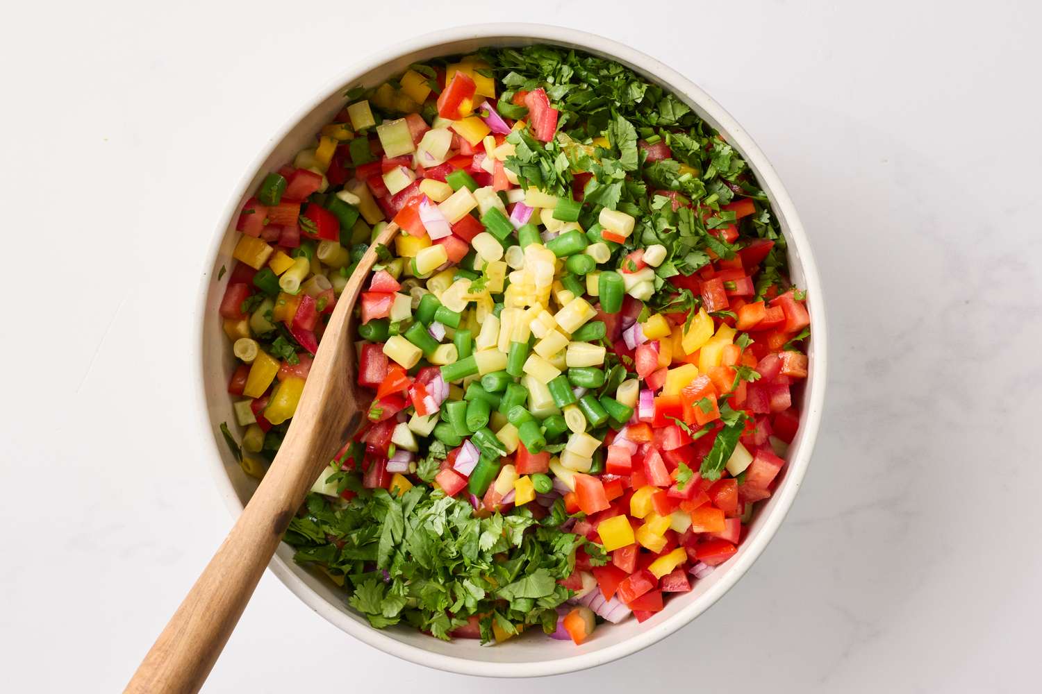 Mixed chopped vegetables in a bowl with a wooden spoon