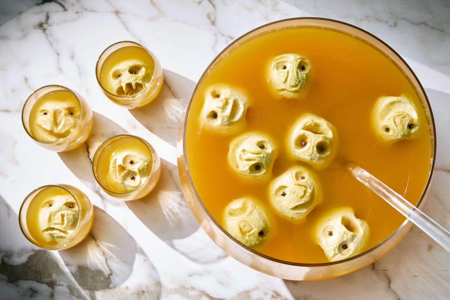 A bowl of cider with carved apple features resembling shrunken heads floating in it cups of similar cider on the side