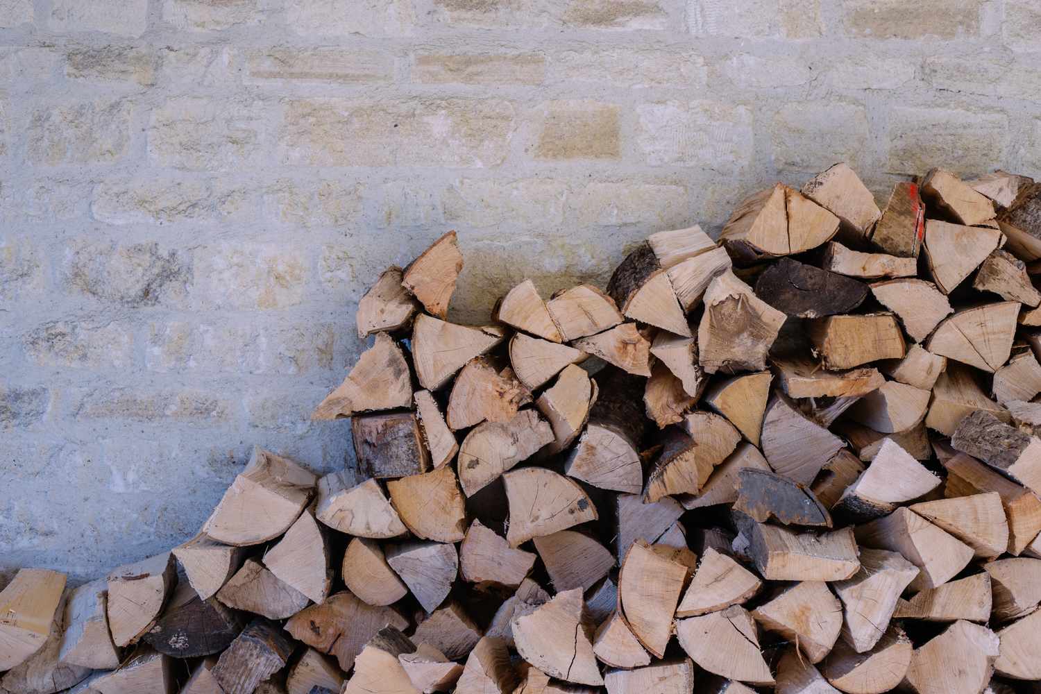 A stack of split firewood against a brick wall arranged in a pile
