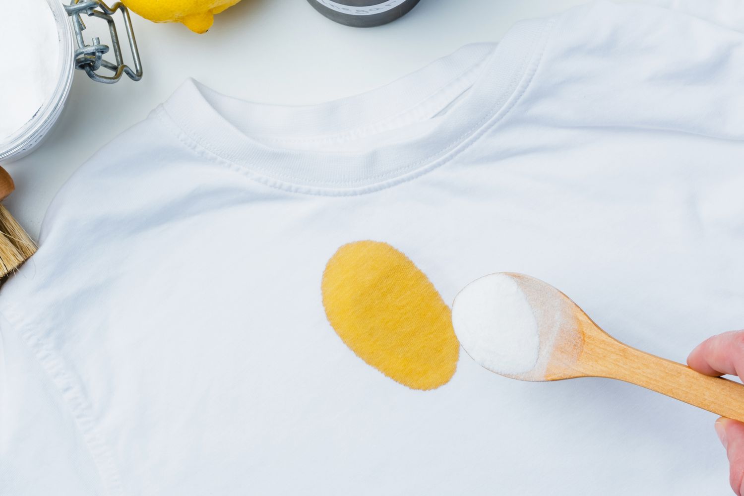 A white shirt with a yellow stain being treated with a wooden spoon containing powder