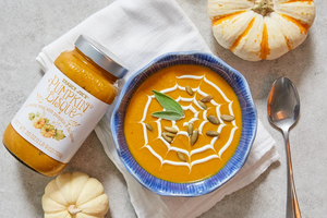 Pumpkin bisque in a bowl with a spiderweb design garnished with seeds and a leaf next to a jar labeled Trader Joes pumpkin bisque