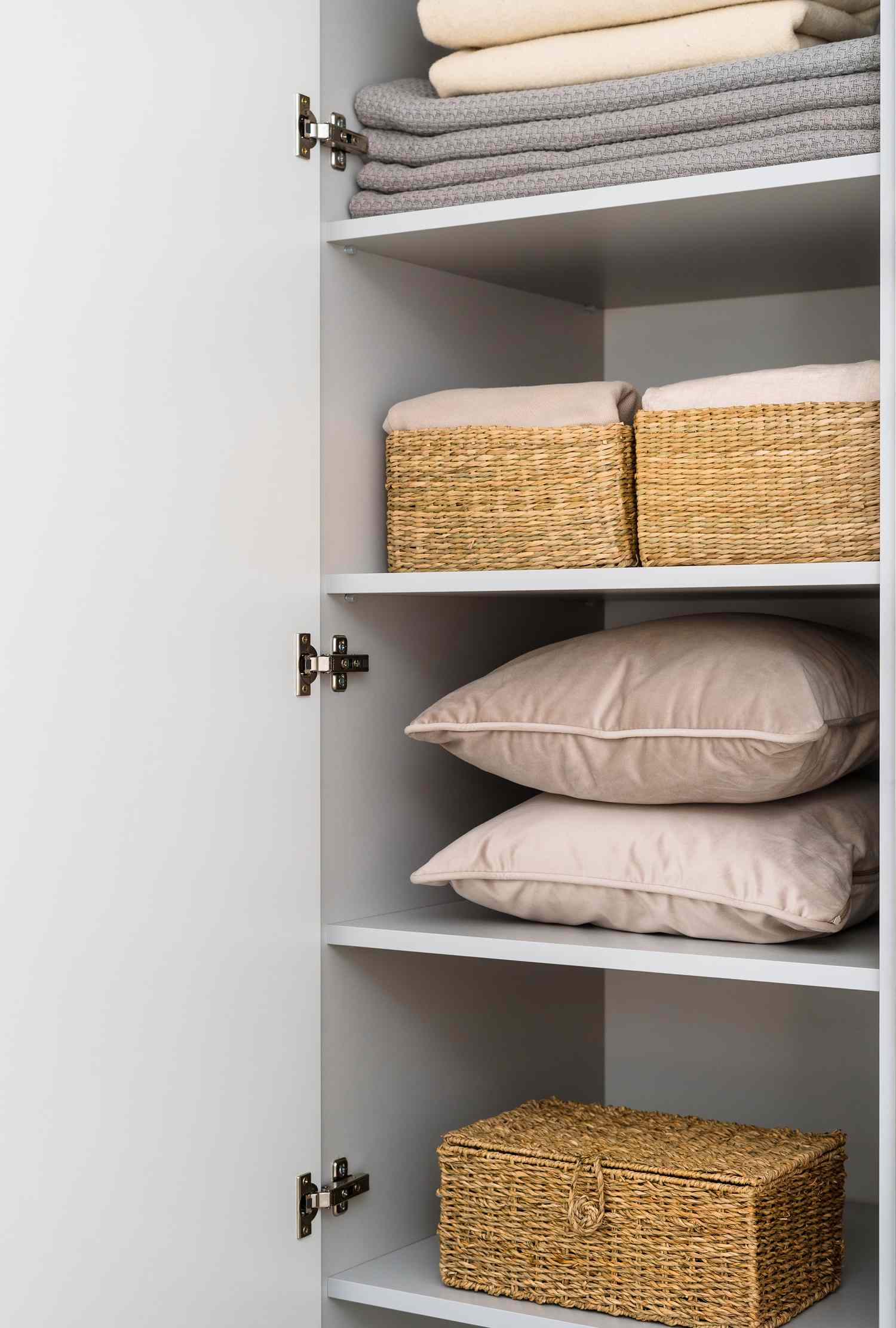 Organized closet shelves with pillows woven storage baskets and folded linens