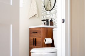 A small bathroom with a wooden vanity cabinet a round mirror and a toilet