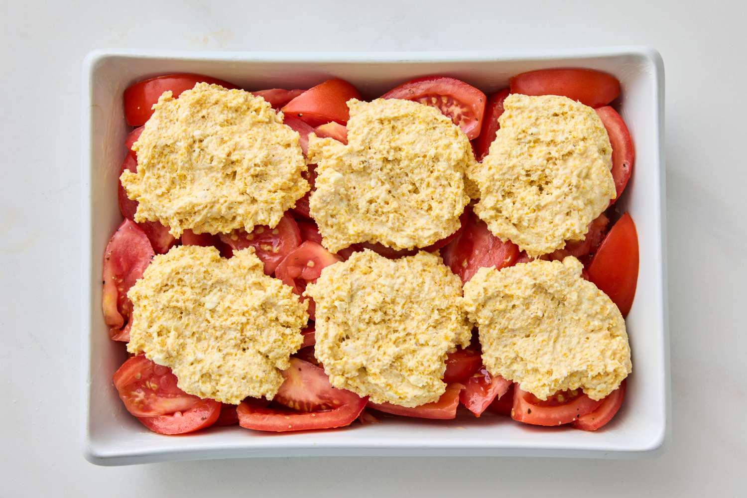A baking dish with tomato slices topped with unbaked biscuit dough pieces
