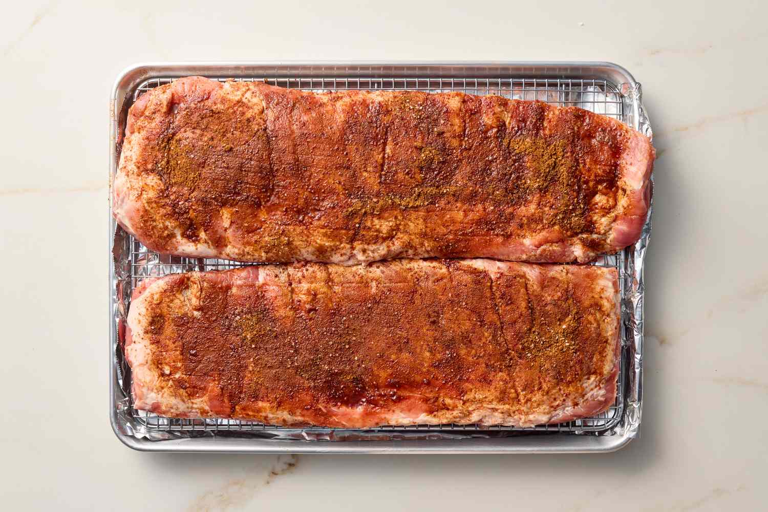 Two racks of seasoned ribs on a baking tray with a wire rack, prepared for oven roasting