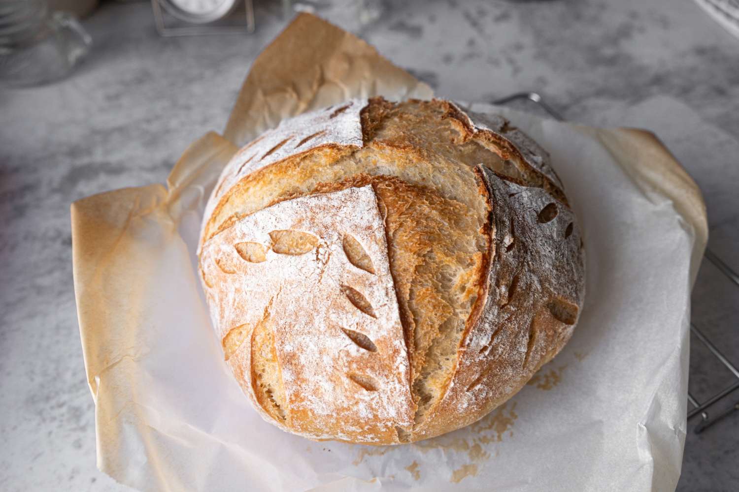 A loaf of artisan bread with decorative scoring resting on parchment paper