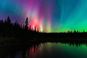 Northern lights above a forest and reflecting in a lake