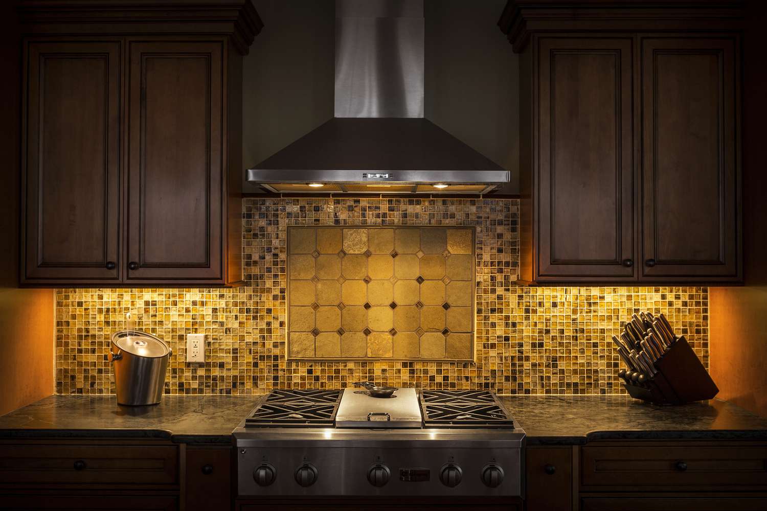 Tile back splash, ventilation hood and stove in dark kitchen