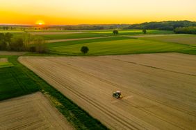 Aerial view of idyllic rural landscape with tractor in field at sunrise. 