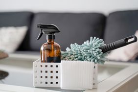 A cleaning kit on a table with a spray bottle a duster and cleaning cloths placed in a small storage container