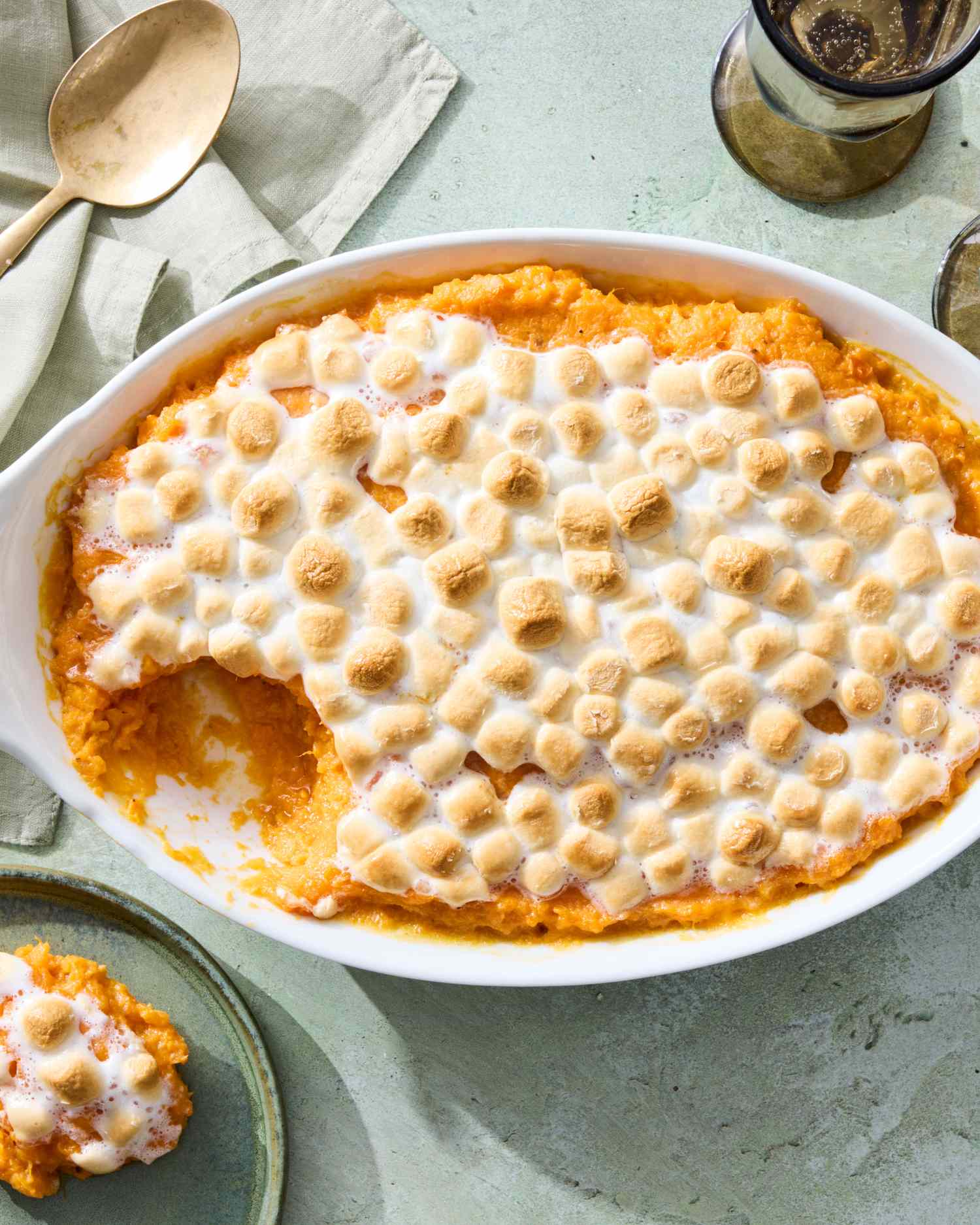 Sweet potato casserole topped with marshmallows in a baking dish with a portion served on a separate plate