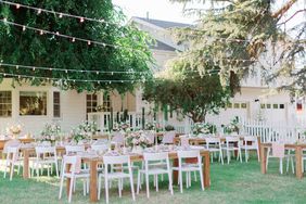 long wooden tables outdoors with white chairs and overhead string lights