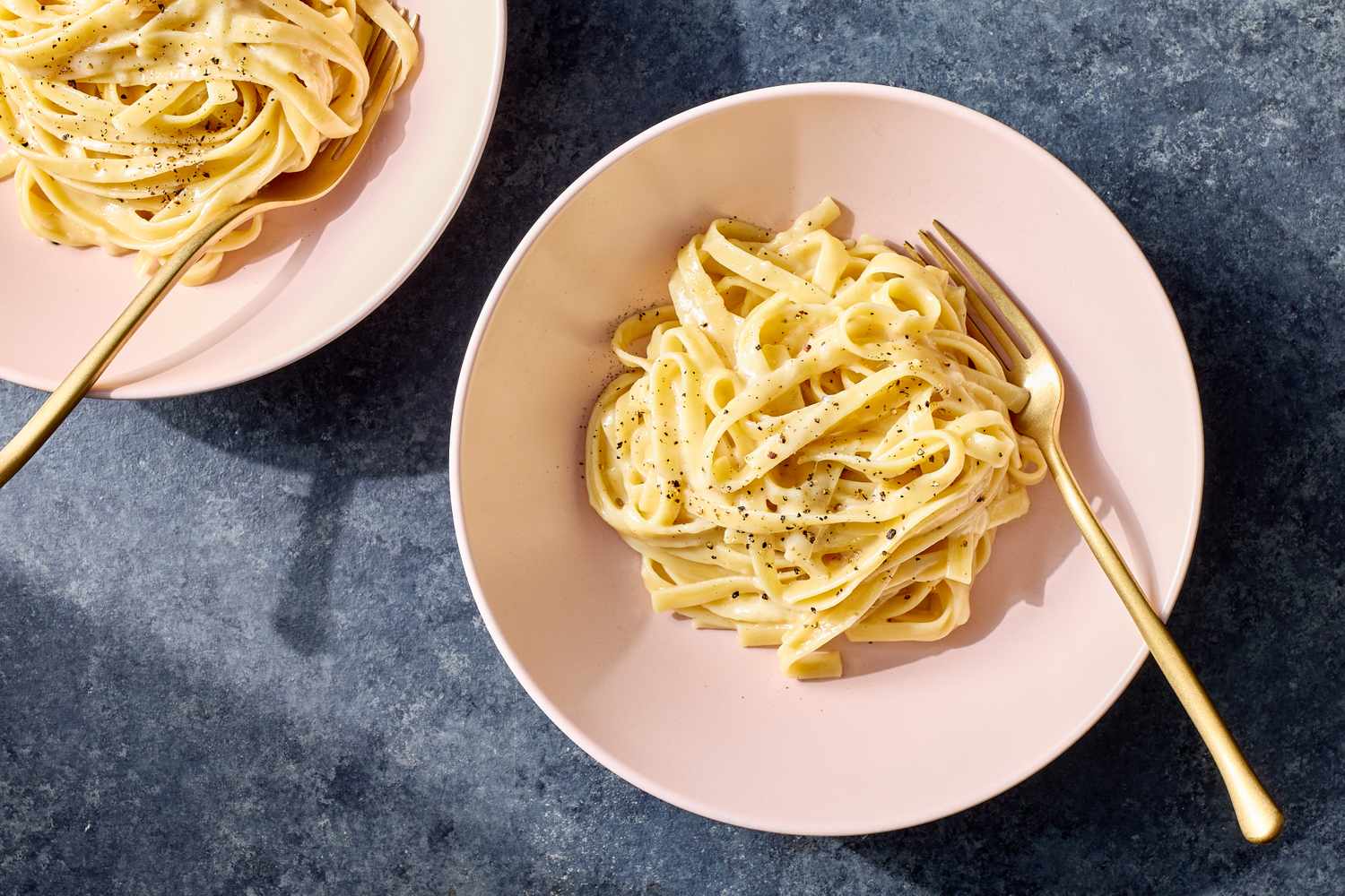 Two servings of fettuccine pasta in a creamy Alfredo sauce served in shallow bowls each with a fork