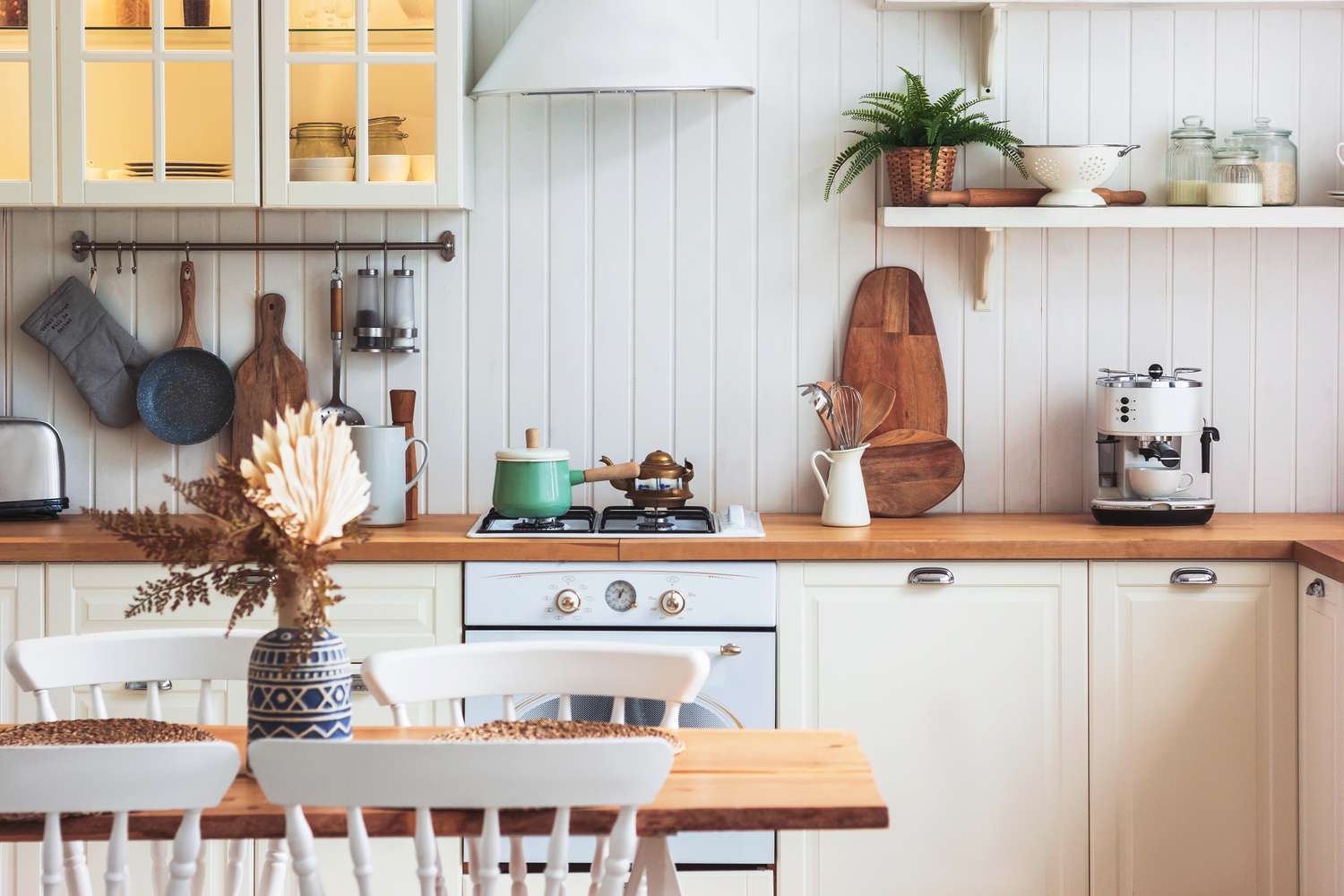 A kitchen interior featuring white cabinets shelves cookware and a dining table with chairs