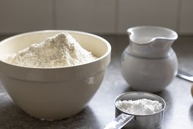 Baking ingredients on a counter including a bowl of flour a measuring cup and a small pitcher