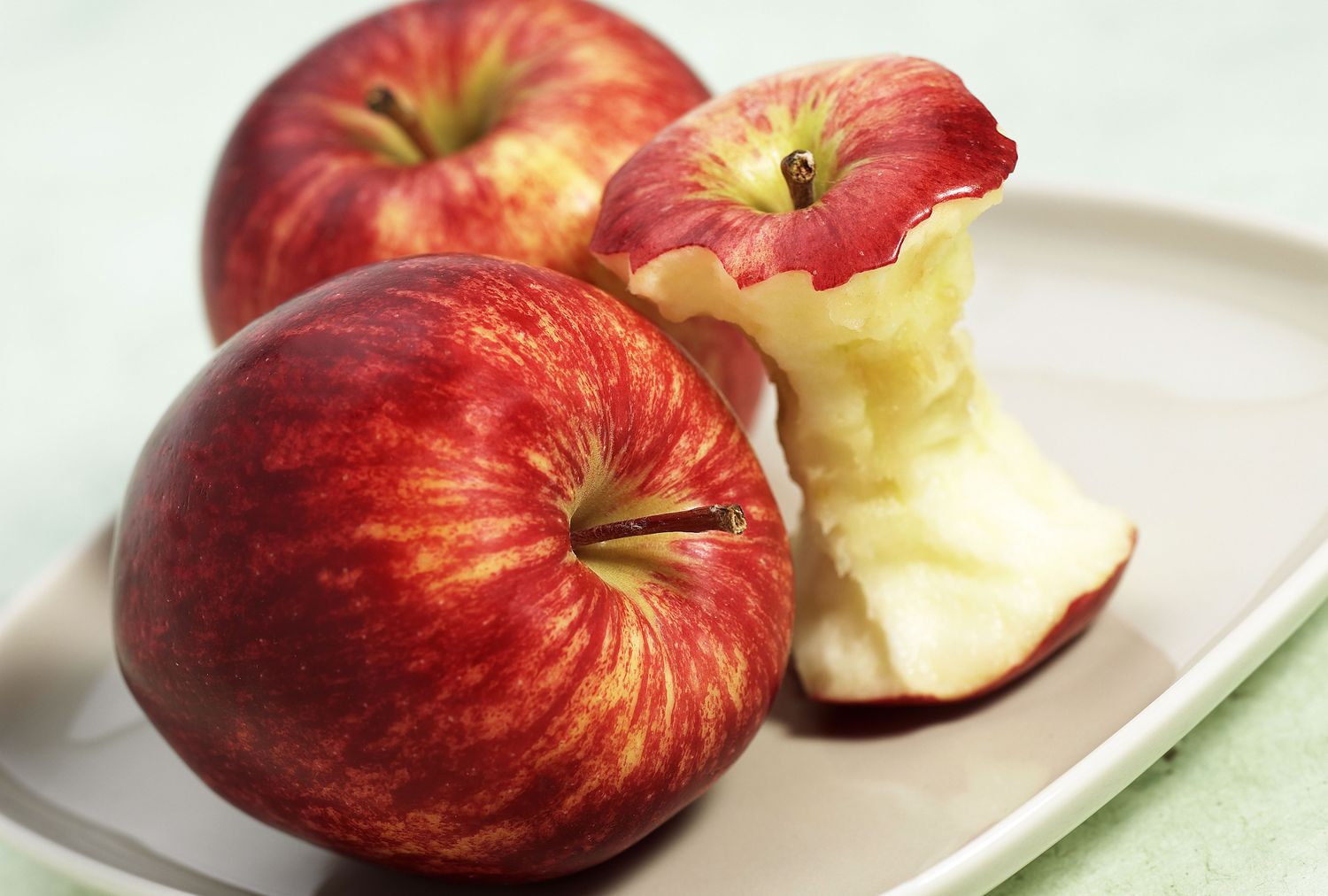 Two whole apples and an apple core on a plate