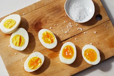 Hardboiled eggs sliced on a wooden cutting board next to a small bowl of salt