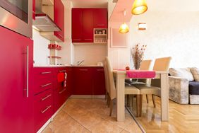 A modern kitchen with red cabinets and dining area with chairs and table