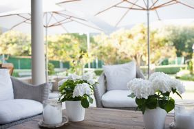 Outdoor seating area with white cushions flowers in pots and large umbrellas providing shade