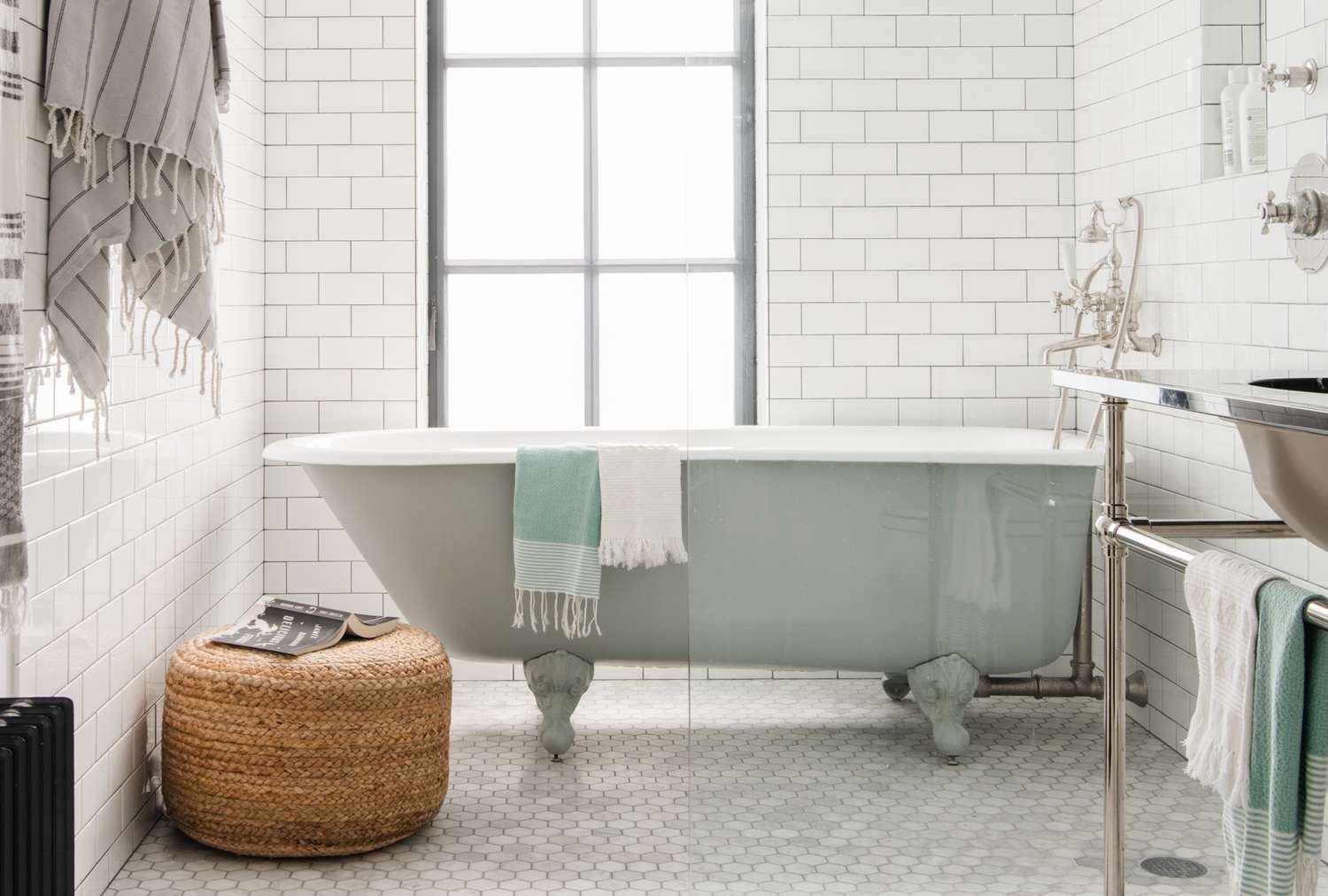 A bathroom with a clawfoot bathtub a wicker stool and towels hanging and folded on fixtures