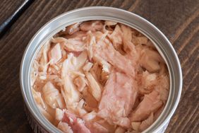 Open can showing chunks of tuna in liquid resting on a wooden surface