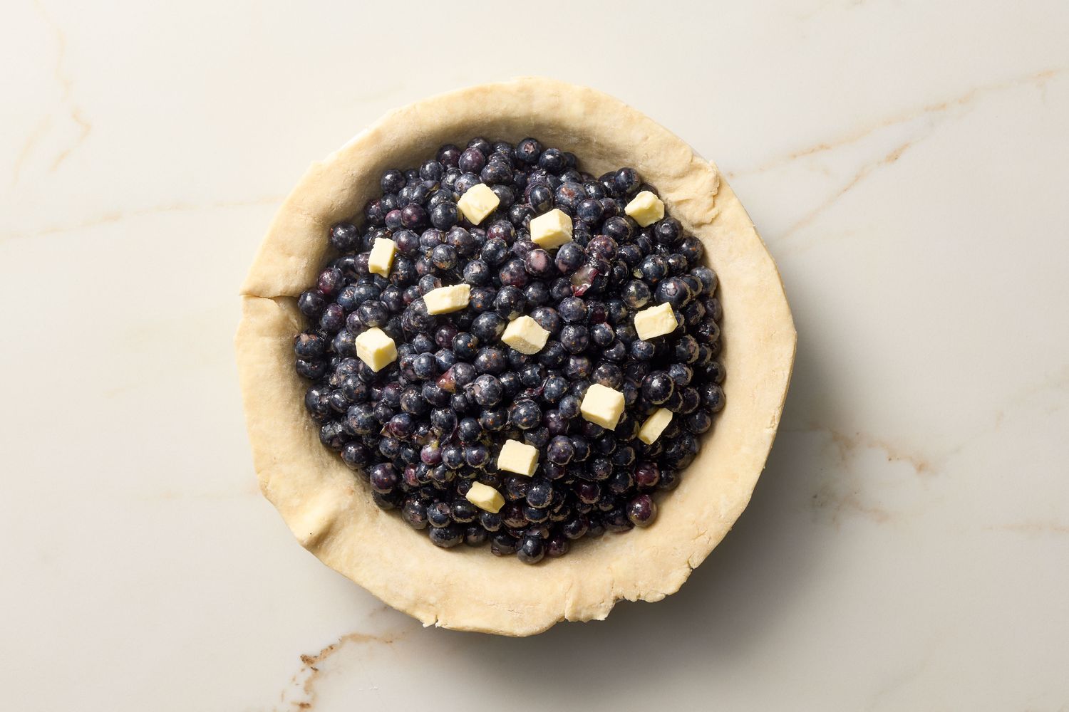 Unbaked blueberry pie with butter pieces on top of the filling