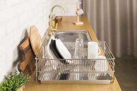 A dish rack beside a sink holding plates a glass and other items