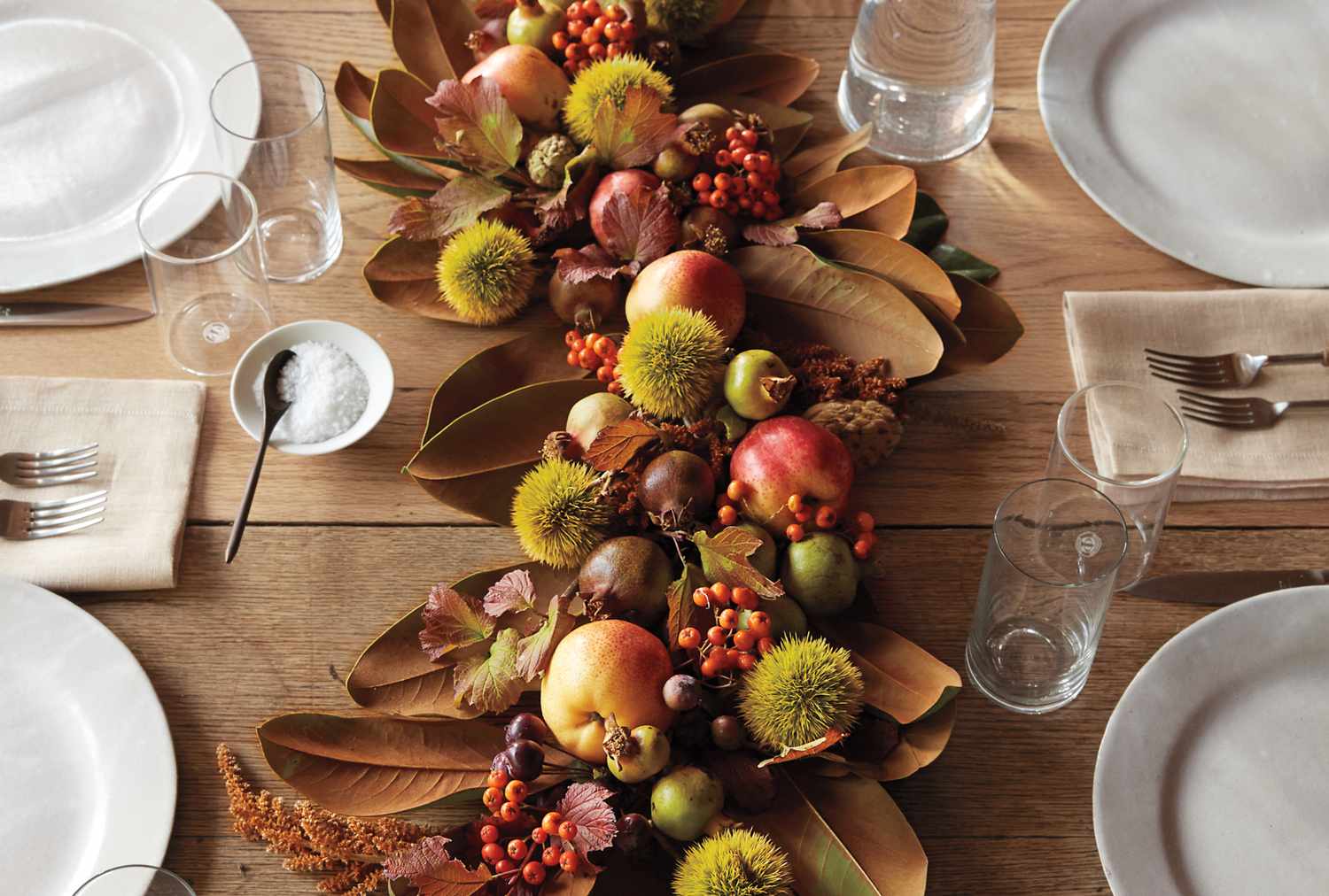 Thanksgiving table centerpiece featuring fruit foliage and decorations with table setting in view