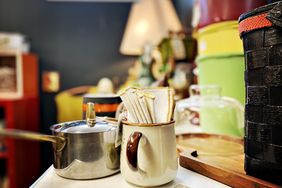A mug containing napkins placed next to a saucepan on a table surrounded by various household items