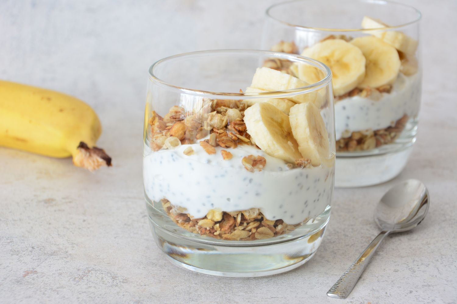 Yogurt parfaits with granola and banana slices served in glasses a spoon and a whole banana on the side