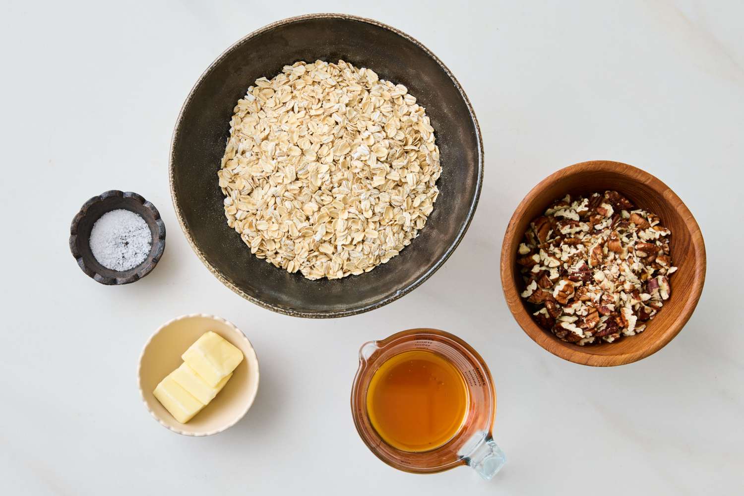 Ingredients for honey pecan granola including oats pecans honey butter and salt arranged in separate bowls