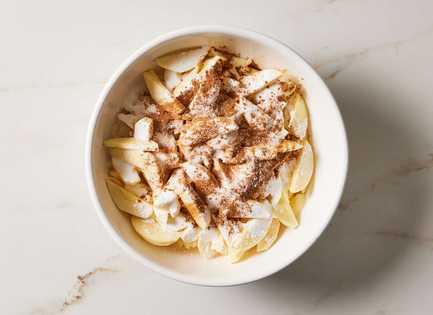 overhead view of sliced apples and spices in a dish on marble surface