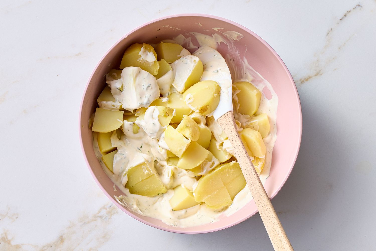 Bowl of potato salad being mixed with a spatula