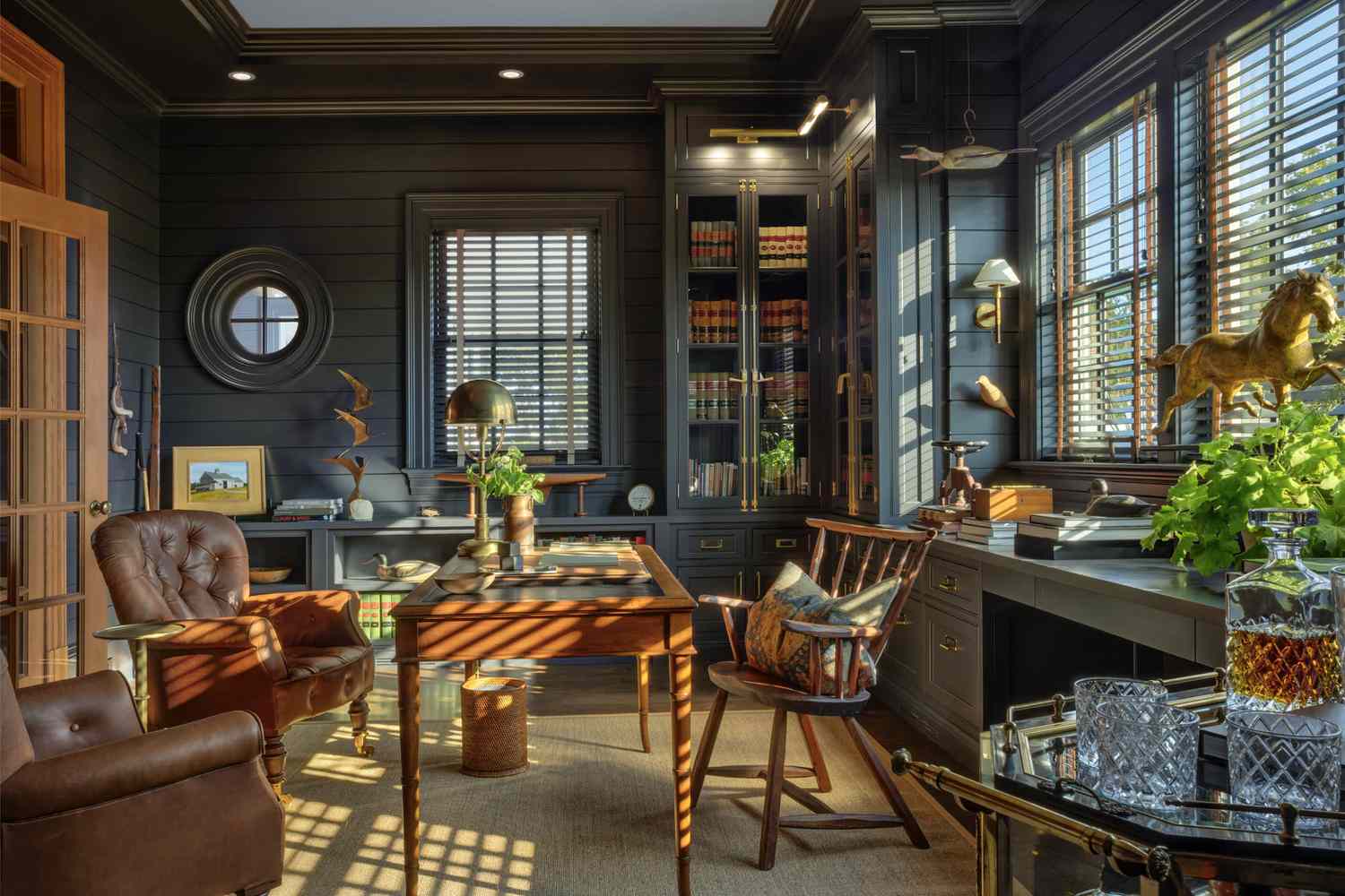 A study with wooden furniture bookshelves and sunlight streaming through window blinds